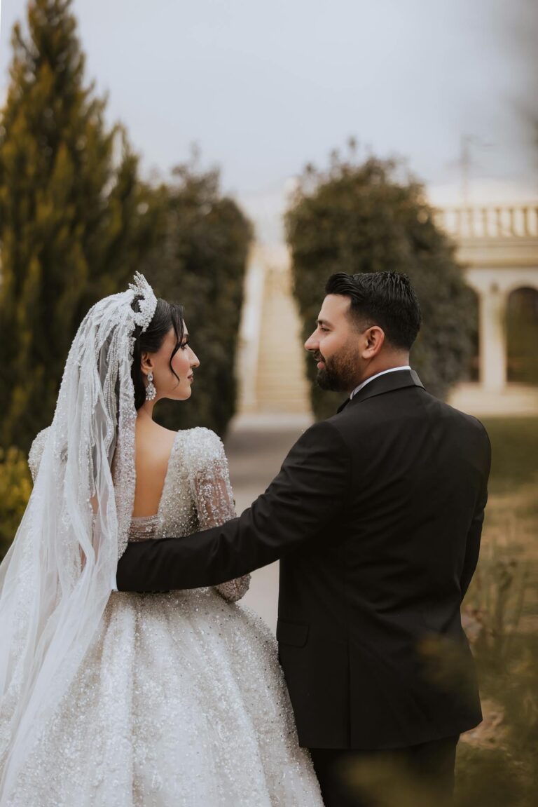 Happy bride and groom walking arm-in-arm in a lush garden setting, showcasing elegant wedding attire.